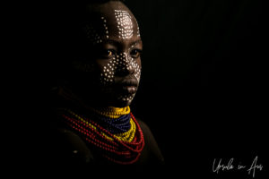 Portrait against black: painted Kara girl in red and yellow beads, Dus Village, Omo Valley Ethiopia