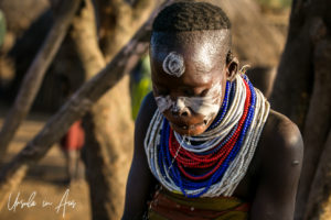Portrait: Kara woman in face paint with liquid streaming from the incision under her lip, Omo Valley Ethiopia
