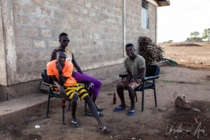Young Kara men seated outside a brick building, Dus Village, Omo Valley Ethiopia