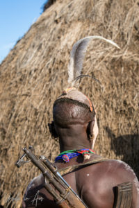 Rear view: Kara man with an AK47 in a Skull Cap and face paint, Dus Village, SNNPR Ethiopia