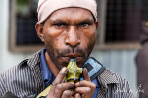 Portrait: Papuan man blowing a painted whistle, Mount Hagen PNG.