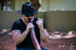 Portrait: Man in black playing a didgeridoo, Ayers Rock Resort NT Australia.