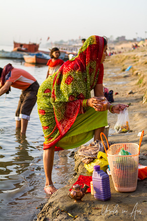 Woman in red and green making offerings to Ganga Ma, Varanasi, India.