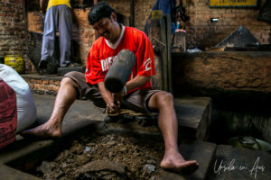 Man with a mallet pounding the dried remains of mustard seeds, Khokana, Nepal