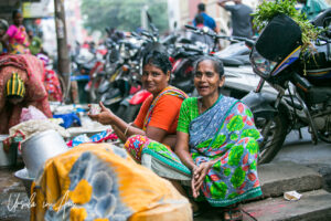 Two women in saris seated in a crowded parking area outside Goubert Market, Puducherry, India.
