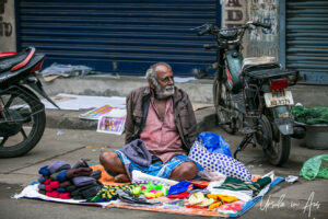 Man seated on the ground with hats for sale, Puducherry, India.