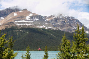 Tiny-looking red lodge against a large snow-capped mountain from Bow Lake Viewpoint, Highway 93N, Banff Alberta Canada