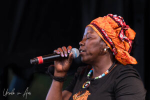 Portrait: One of Les Aunties, in black and orange, on stage singing, Vancouver Island Musicfest, Comox BC Canada