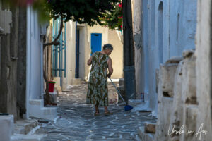 Greek woman in a flowered dress sweeping a laneway, Parikia, Paros Greece.