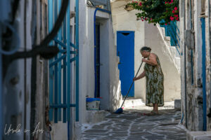 Greek woman in a flowered dress sweeping a laneway, Parikia, Paros Greece.