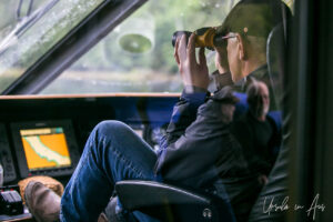 Man with binoculars on the bridge of a boat, Khutzeymateen Chanel, BC Canada