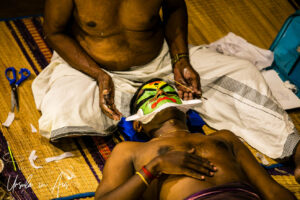 Hands applying a Chutti to Arjunan, Great K V Kathakali Center in Fort Kochi, Kerala India