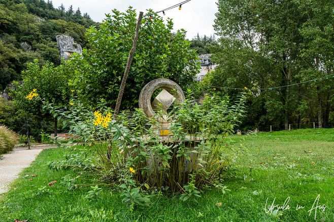 Plants overgrowing an circular stone marker, Bouziès Halage parking, France.