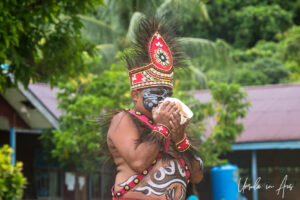 Young man in face paint and in traditional costume blowing a conch shell, Kwatisore, Papua Indonesia
