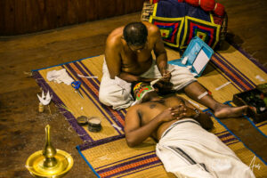A man applying paste to another man's face, Kerala Kathakali Centre, Fort Kochi, India