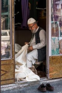 Man in a topi with reams of cloth, Srinagar, Jammu and Kashmir, India.