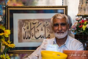 Man in front of Arabic script, Jamia Market, Srinagar Nowhatta, Jammu and Kashmir, India.