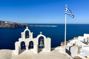Four bells and a Greek flag against the caldera, Oia Santorini.