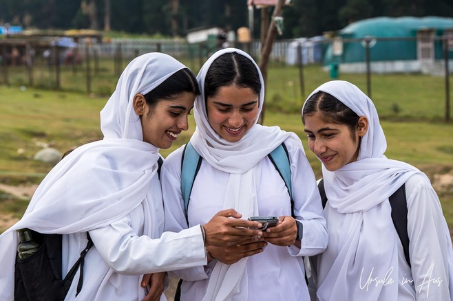 Three young women in white hijabs looking at a phone, Doodhpathri, India