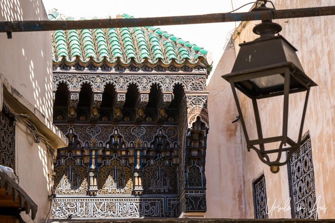 A metal lantern in front of an ornate wooden building, Fes el Bali, Fes, Morocco.